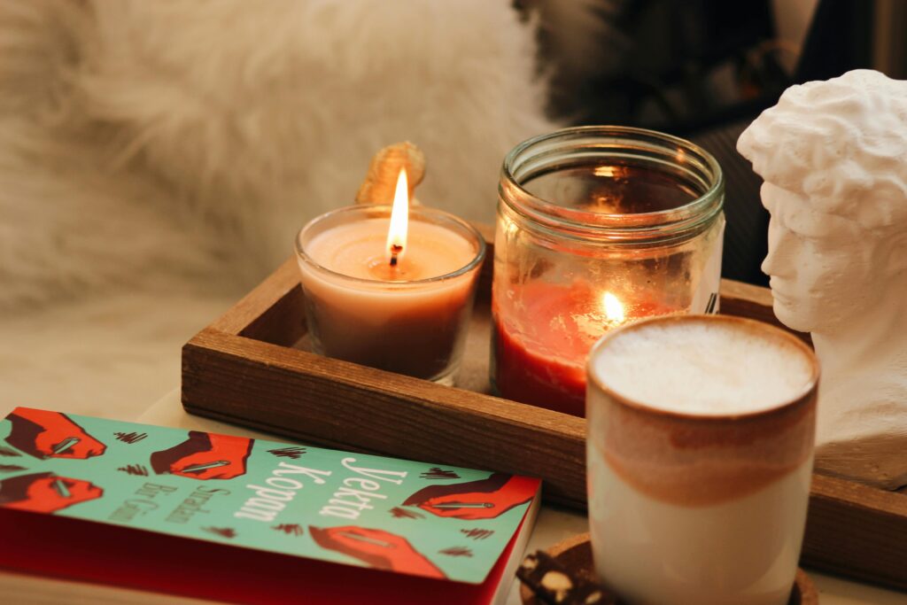 A cozy setup with a book, candles, and a coffee cup in warm lighting.