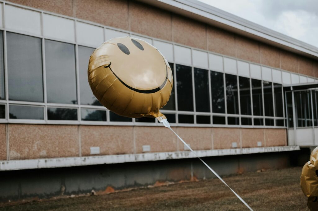 A cheerful yellow smiley balloon floating outdoors in front of a modern building.