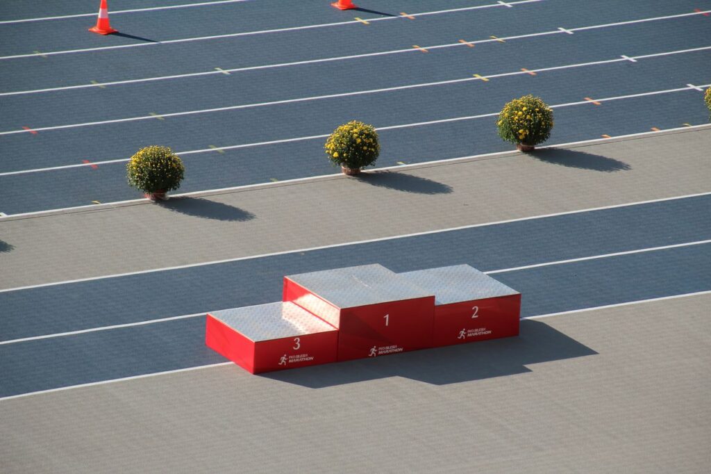 ▲ Red podium on a sunny outdoor athletics track with decorative plants.